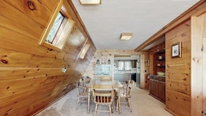 A wooden interior with a dining table and chairs, a kitchen area, and a window. - Comfy Lakefront Cabin with Gorgeous Views, Private Dock & Pebble Beach (Lily Bay Township)