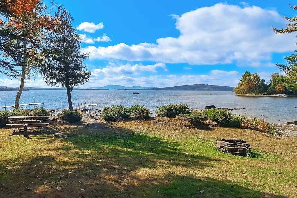 A lakeside view with a picnic table, a fire pit, and a boat on the water.