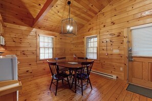 Ein Holzblock-Interieur mit Esstisch, Stühlen, einer Pendelleuchte und einer Tür mit Fenster.