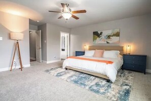 Ein Schlafzimmer mit Bett, Deckenventilator, Nachttisch, Lampe und einem Bild an der Wand.