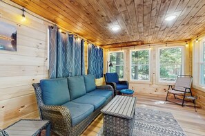 A log cabin interior with a sofa, chairs, a table, and large windows. - Lakefront cabin close to town with dock, firepit - dogs welcome (Beaver Cove)