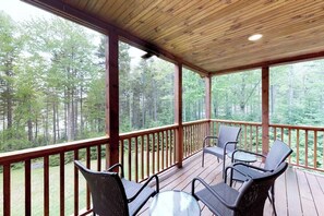 Eine überdachte Terrasse im Freien mit Holzgeländern, zwei Korbstühlen und einem Glastisch.