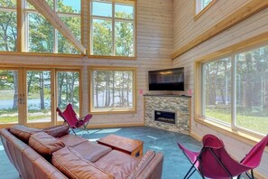 Eine Hütte mit großen Fenstern, einem Kamin aus Stein, Ledersofas und einem Flachbildfernseher.