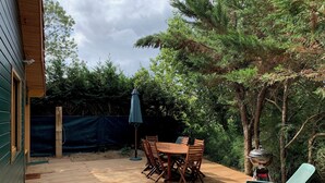 A wooden deck with a table and chairs, a grill, and a covered umbrella. - Wooden beach house for vacations - Le Verdon-sur-Mer (33) (Le Verdon-sur-Mer)