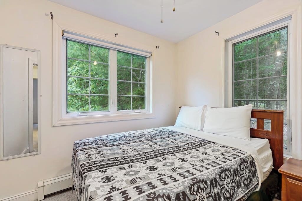 A bedroom with a bed, two windows, and a nightstand.