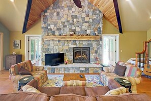 A cozy living room with a stone fireplace, comfortable seating, and a television. - Renovated waterfront cottage with expansive deck, multiple fireplaces, & grill (Lamoine)