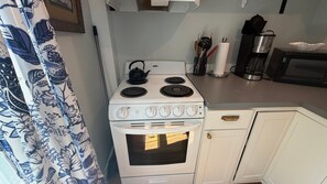 Una cocina con estufa, horno y microondas blancos. Hay un hervidor sobre la estufa, y se observan utensilios de cocina.