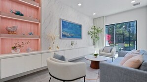Una sala de estar moderna con un sofá, sillones, una mesa de centro y un estante decorativo con diversos objetos.