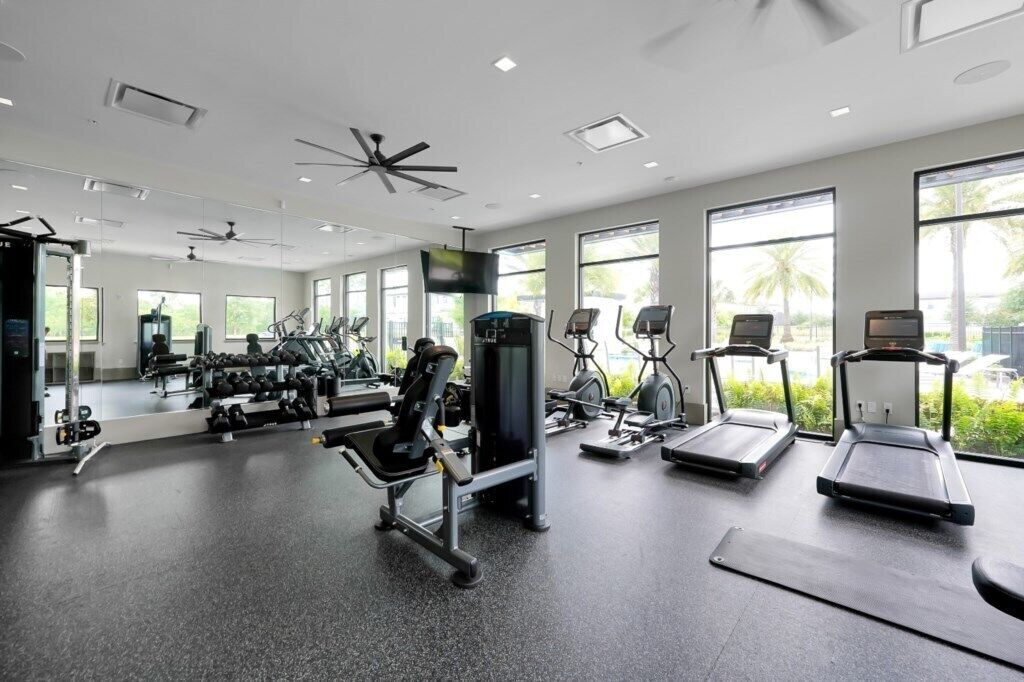 Une salle de sport équipée de matériel d’exercice, dotée de grandes fenêtres et d’un ventilateur de plafond.