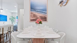 Comedor con una mesa redonda para seis personas, sillas blancas y un florero con flores rosadas.
