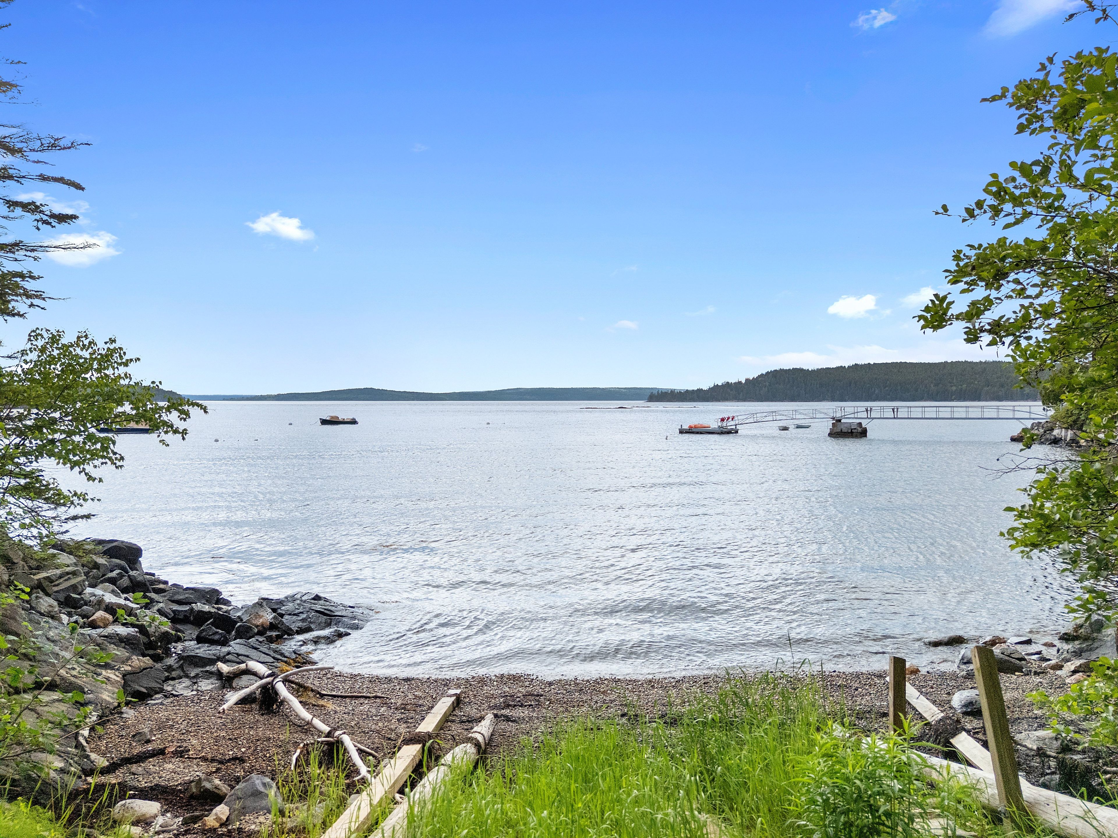 A calm body of water with boats, a wooden dock, and a forested hill in the background.