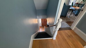 A staircase with a wooden handrail and a white balustrade leading to a room with a wooden floor and a door. - Comfortable Getaway for Two w/ Kitchenette - Right in the Heart of Downtown (Castine)