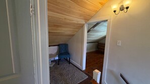 A room with a wooden ceiling, a blue chair, a white door, and a light fixture on the wall. - Comfortable Getaway for Two w/ Kitchenette - Right in the Heart of Downtown (Castine)