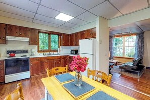 A kitchen with wooden cabinets, a dining table with placemats, and a vase with flowers. - Comfortable Castine getaway w/ a full kitchen - walk to the waterfront (Castine)