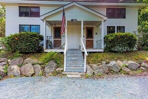 A two-story house with a porch, a flag, and a staircase leading to the front door. - Comfortable Castine getaway w/ a full kitchen - walk to the waterfront (Castine)