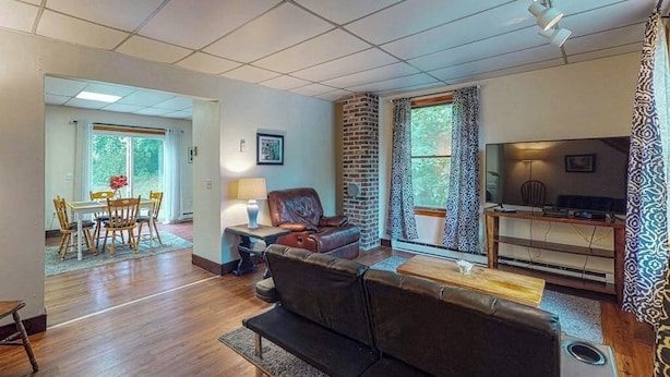 Een woonkamer met een bank, een televisie, een open haard en een eethoek met een tafel en stoelen.