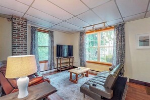 A living room with a sofa, a coffee table, a TV stand, and a lamp. - Comfortable Castine getaway w/ a full kitchen - walk to the waterfront (Castine)