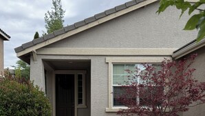 Une maison d’habitation avec une allée en béton, une porte d’entrée, une fenêtre et un petit arbre aux feuilles rouges.