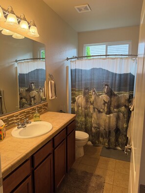 Un baño con un espejo grande, un lavabo, un inodoro y una cortina de ducha con estampado de caballos.