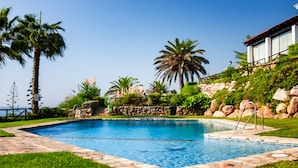 Ein Swimmingpool mit Steinrand, umgeben von Palmen und einer Steinmauer.