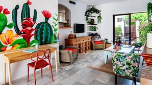 Ein modernes Wohnzimmer mit einem Holztisch, Korbstühlen, einem Fernseher und einem großen Fenster mit Blick auf Grünflächen.