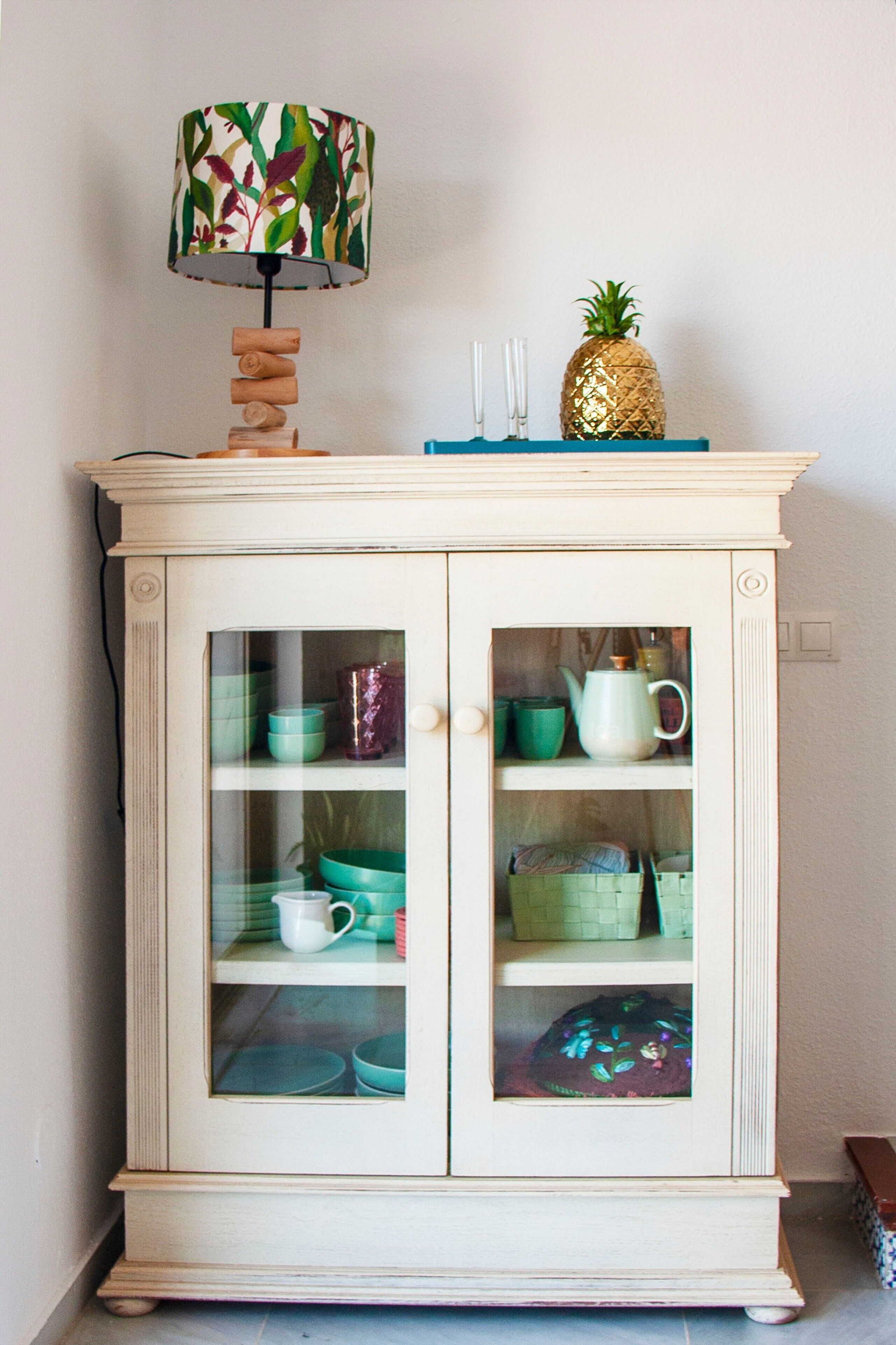 A cabinet with glass doors, a lamp, and a pineapple decoration.