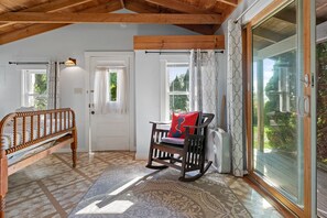 A room with a wooden ceiling, a rocking chair with a cushion, a bed, and a large window with curtains. - Atlantic Gardens 1- Multi-unit with oar & boat house with private dock & kayaks (Boothbay Harbor)