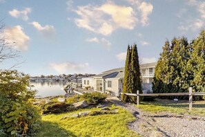 A lakeside property with a pathway leading to a building, surrounded by greenery and a clear sky.