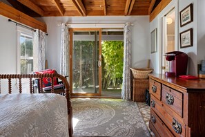 A room with a bed, a dresser, a chair, a window with curtains, and a view of greenery outside. - Atlantic Gardens 1- Multi-unit with oar & boat house with private dock & kayaks (Boothbay Harbor)