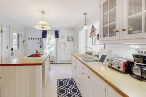 A kitchen with a central island, a stove, a toaster, and a coffee maker. There are cabinets with glass doors, a hanging light fixture, and an American flag.