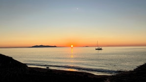 A calm sea at sunset with a sailboat anchored in the distance. - Black Sand Santorini Studio (Perissa)