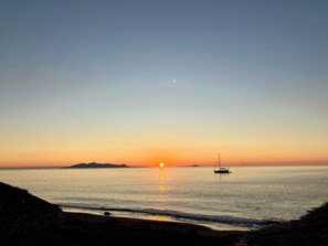 A calm sea at sunset with a sailboat anchored in the distance. - Black Sand Santorini Studio (Perissa)
