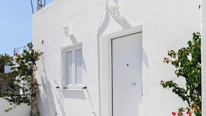 A white building with a door, a window with shutters, and a small balcony. - Black Sand Santorini Studio (Perissa)