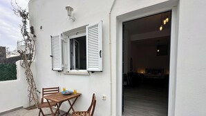 A balcony with a table, chairs, and a bowl of fruit. - Black Sand Santorini Studio (Perissa)