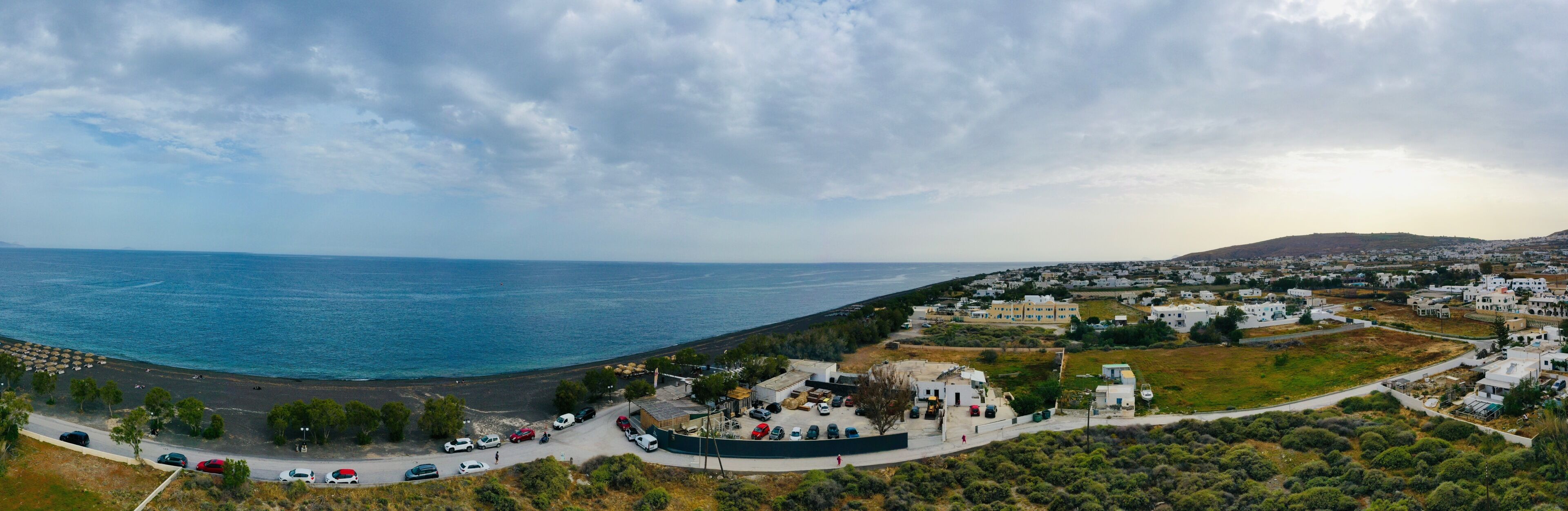 A coastal town with a beach, parked cars, and white buildings.