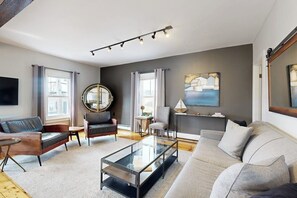 A modern living room with a glass coffee table, leather sofas, a round mirror, and artwork on the walls. - Head of the Harbor- Nautical vacation rental in in walkable downtown with harbor view, grill & deck (Boothbay Harbor)