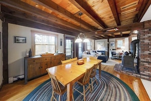 A wooden dining table with chairs, a kitchen area with cabinets, a brick fireplace, and a living room with a sofa and a coffee table.