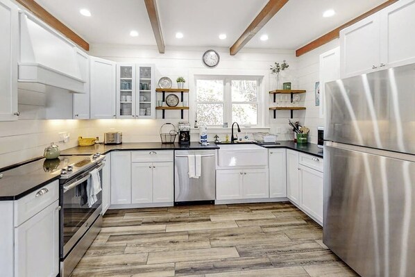 A modern kitchen with white cabinets, a stainless steel refrigerator, and wooden flooring. - Boothbay Cottage- Coastal home with new, full kitchen, walkable downtown location (Boothbay Harbor)