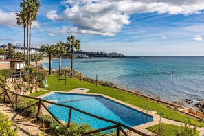 Ein Pool mit Blick auf das Meer, Palmen und eine entfernte Küste.