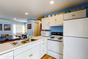 Una cocina con armarios blancos, estufa, microondas y refrigerador.
