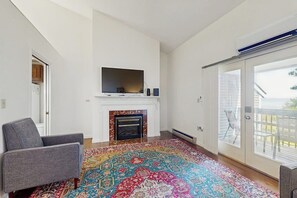 Ein Wohnzimmer mit Kamin, Flachbildfernseher, gemustertem Teppich und einer Glastür zu einem Außenbereich.
