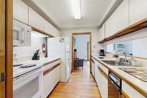 A compact kitchen with white cabinets, a microwave, a refrigerator, a stove, and a sink. - Townhome w/ Bonus Loft, High-Speed WiFi, Partial AC & Full Kitchen (Bar Harbor)