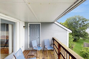 A covered porch with a wooden railing, a sliding glass door, and two chairs. - Townhome w/ Bonus Loft, High-Speed WiFi, Partial AC & Full Kitchen (Bar Harbor)