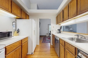 A kitchen with wooden cabinets, a microwave, a refrigerator, and a sink. - Convenient Dog-Friendly Townhouse w/Bay Views, Fast WiFi, A/C, Gas Grill, & More (Bar Harbor)