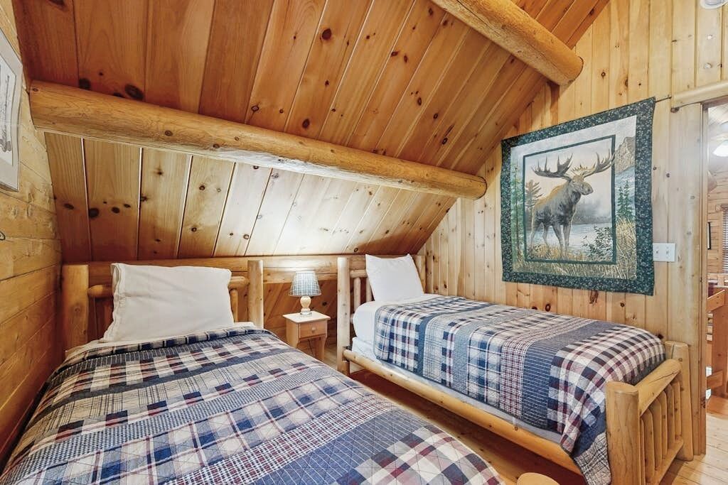 A cabin with two wooden beds, a wooden ceiling, and a framed moose picture on the wall.