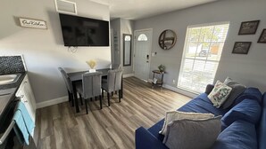 Cozinha moderna com área de refeições, sala de estar com sofá azul e uma janela grande com persianas.
