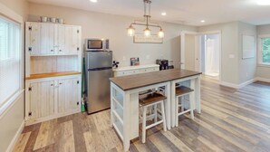 Une cuisine avec une table en bois, des placards blancs, un réfrigérateur et un four à micro-ondes.