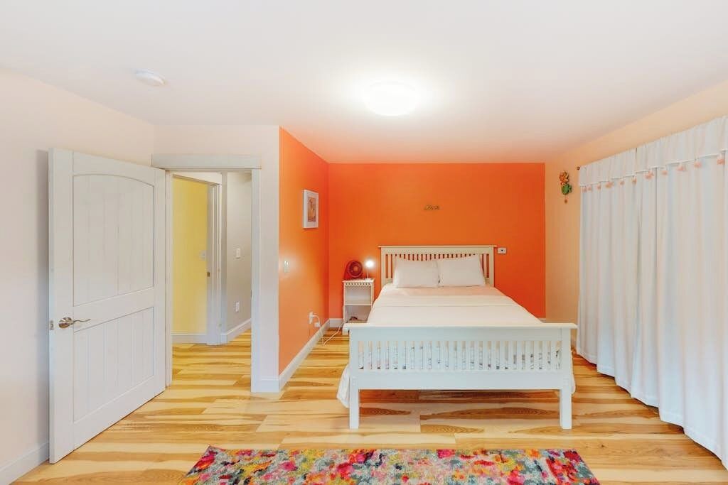 A bedroom with a bed, a nightstand, a door, and a window with curtains.