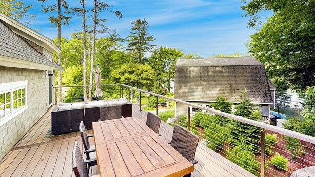 Een houten terras met een tafel en stoelen, omringd door groen en een huis.
