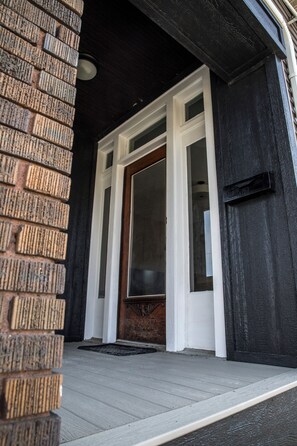 A wooden door with a glass panel, a brick wall, and a white door frame. - Spacious 3-bedroom apartment ground floor in marvellous Evansville with AC (Evansville)